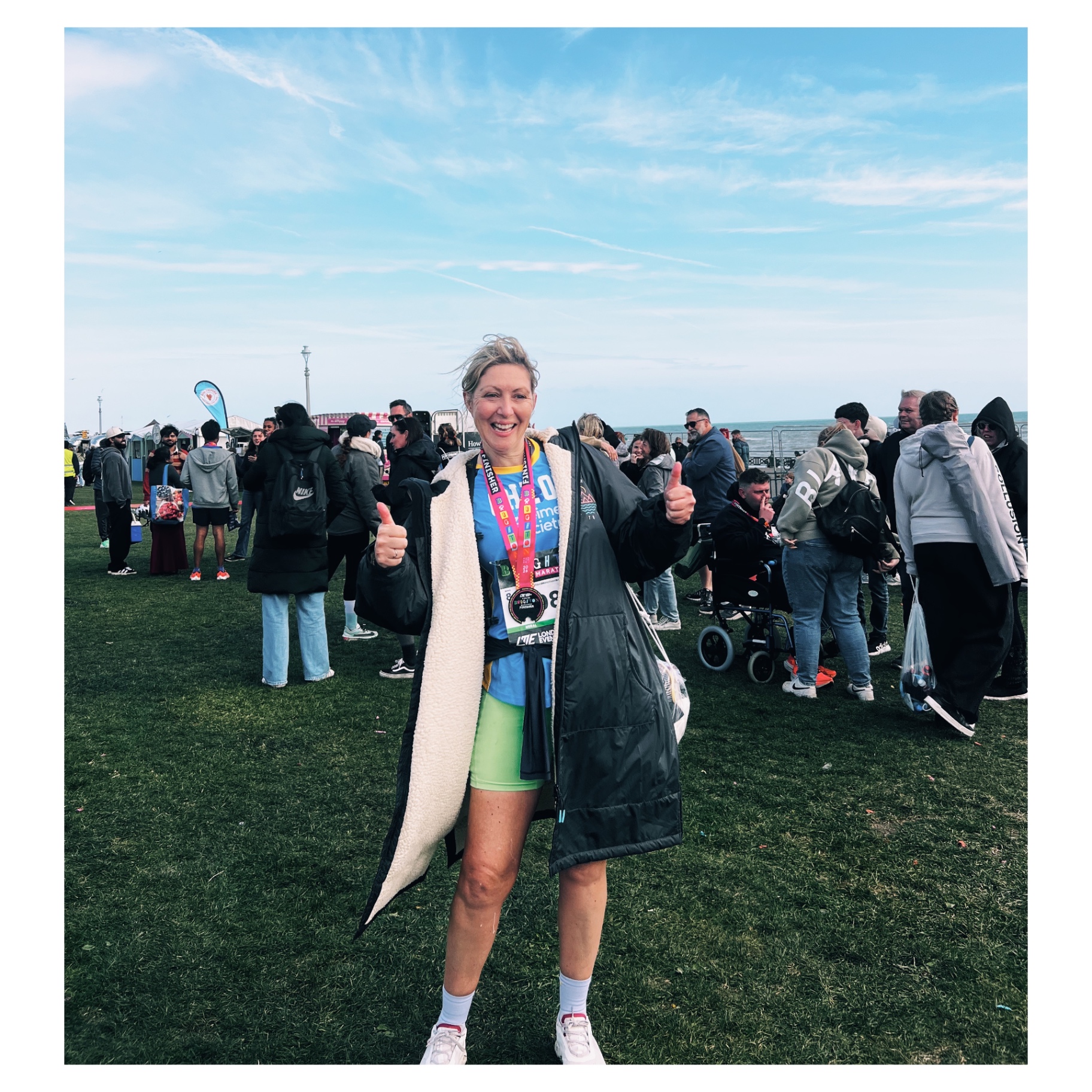 Smiling marathon finisher with medal on Brighton seafront, giving two thumbs up